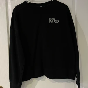 Svart sweatshirt med text - Säljer en svart sweatshirt med texten 'MON PARIS' i vita bokstäver på bröstet. Tröjan är långärmad och har en avslappnad passform. Perfekt för en casual look eller mysiga dagar hemma. 🖤