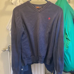 Mörkblå tröja från Morris - Säljer en snygg mörkblå tröja från Morris i storlek XS. Tröjan har en v-ringad design och ett litet rött emblem på bröstet. Perfekt för både höst och vinter, och den är i mycket bra skick. Passar bra till både vardag och lite finare tillfällen.