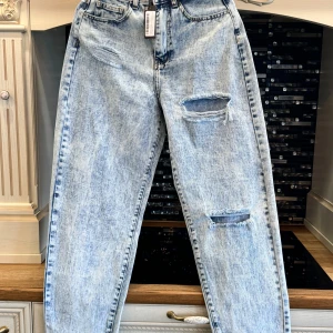 Ljusa jeans från PrettyLittleThing - Säljer ett par ljusa jeans från PrettyLittleThing i nytt skick. De har en cool, sliten look med revor på framsidan och en hög midja. Perfekta för en avslappnad stil! 🕶️