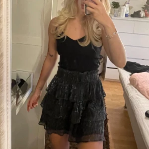 Svart glittrig kjol från ONLY - Säljer en superfin svart glittrig kjol från ONLY i storlek M. Kjolen har flera lager med volanger och ett elastiskt midjeband för en bekväm passform. Perfekt för festliga tillfällen eller en utekväll! ✨