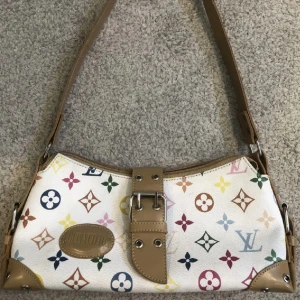 Vit axelväska med färgglatt mönster - Säljer en super snygg vit axelväska (ej äkta). Väskan har bruna läderdetaljer och är i okej skick . Perfekt för att liva upp vilken outfit som helst! 👜✨ köparen står själv för frakten samt att priset går alltid att diskutera 🥰