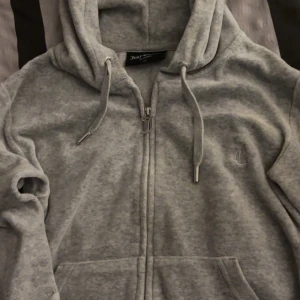 Grå velour zip up hoodie från Juicy Couture - Mysig grå velour zip up hoodie från Juicy Couture i storlek XS. Den har en dragkedja med ett snyggt J-hänge och justerbara snören i huvan. Perfekt för en avslappnad stil eller mysiga dagar hemma. 💖 Nypris: 1300kr, jätte bra skick. Säljer för 750kr men pris kan diskuteras