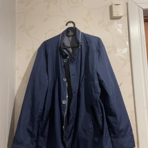 Mörkblå jacka med knappar - Säljer en stilren mörkblå jacka i bra skick. Den har långa ärmar och stängs med knappar framtill. Perfekt för höst och vår, med en klassisk look som passar både till vardags och lite finare tillfällen.
