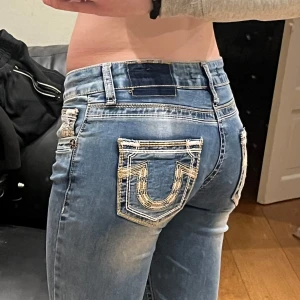 Blå jeans med broderade fickor - Säljer ett par snygga blå jeans med coola broderade detaljer på bakfickorna. Har en låg midja, perfekt för en casual look. Jeansen har en klassisk femficksdesign och är i bra skick. Perfekta för både vardag och fest! Innerben:77. Midja:35.