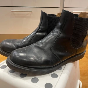 Svarta Chelsea boots från Dr. Martens - Säljer ett par klassiska svarta Chelsea boots från Dr. Martens. De är i skinn och har den typiska elastiska panelen på sidan för enkel på- och avtagning. Skorna har en robust sula som är oljeresistent. Perfekta för både höst och vinter!