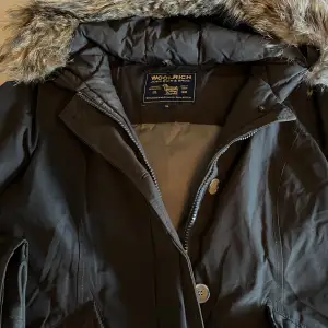 Säljer en brun parkajacka från Woolrich i mycket bra skick. Jackan har en mysig pälsfodrad huva och långa ärmar. Perfekt för kalla vinterdagar med sin varma och skyddande design. Den har både dragkedja och knappar för extra skydd mot kyla. Passar perfekt för vinterns alla äventyr! ❄️