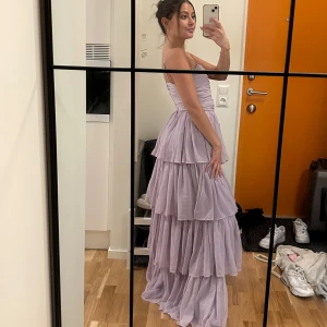 Ljuslila långklänning med volanger - Säljer en superfin ljuslila långklänning med volanger. Den har smala axelband och en snygg cut-out detalj framtill. Perfekt för bröllop eller bal! 