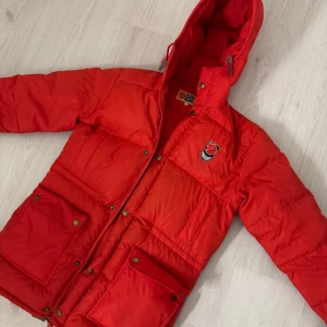 Röd dunjacka från Fjällräven - Säljer en snygg röd dunjacka från Fjällräven i storlek S. Jackan har en praktisk huva och stängs med dragkedja och knappar. Super fint skick, kan behövas en tvätt men inget måste 