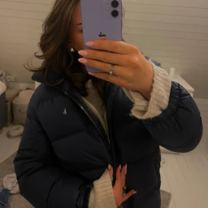 Mörkblå dunjacka från Ralph Lauren - Säljer en snygg och varm mörkblå dunjacka från Ralph Lauren. Jackan har en dragkedja framtill och är perfekt för vintern, den är i bra skick och har en klassisk design med det ikoniska Ralph Lauren-logotypen på bröstet. Defekterna som jackan har är att märket på brötet har nötts lite, den är fortfarande silvrig men själva reflekten av den är borta på vissa ställen. Jackans ena ficka har också en trasig dragkedja men inget jag stört mig på! 