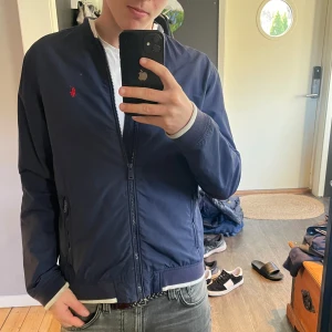 Mörkblå bomberjacka från Ralph Lauren - Säljer en snygg mörkblå bomberjacka från Ralph Lauren. Jackan har en dragkedja framtill och en liten röd broderad logga på bröstet. Perfekt för vår och höst! Den är i mycket bra skick och passar till både vardag och fest. Storlek xl ungdom passar xs