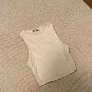 Vit ribbad linnetopp från Zara - Säljer en stilren vit ribbad linnetopp från Zara. Perfekt för sommardagar eller som ett basplagg i garderoben. Toppen är ärmlös och har en tight passform som framhäver figuren. Den är i mycket bra skick och redo för nya äventyr!