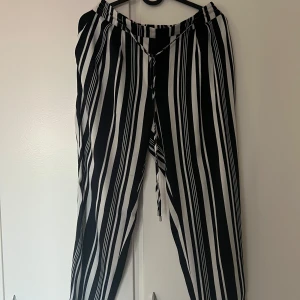 Svartvita randiga byxor - Säljer ett par snygga svartvita randiga byxor i loose fit från Zara. Perfekta för både vardag och fest! De har en bekväm passform med elastisk midja och knytband framtill. Materialet känns lätt och luftigt, vilket gör dem idealiska för vår och sommar.