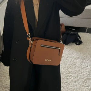 Brun valentino axelväska  - Säljer en snygg brun axelväska med en praktisk dragkedja framtill. Perfekt för vardagsbruk och passar till de flesta outfits. Väskan har en justerbar rem och är i mycket bra skick.