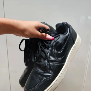 Svarta Nike sneakers - Säljer ett par svarta Nike sneakers i bra skick. De har en klassisk design med snörning och vit sula. Perfekta för vardagsbruk eller träning. Storlek EU 40, UK 6, US 8.5. 