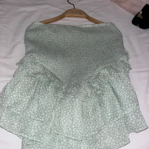 Grön volangkjol från Gina Tricot - Säljer en superfin grön volangkjol från Gina Tricot. Kjolen har ett diskret mönster och flera lager volanger som ger en härlig rörelse. Perfekt för sommardagar eller en festlig kväll. Den är i bra skick och redo för nya äventyr! 🌿