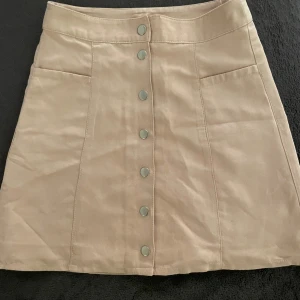 Rosa kjol med knappar - Säljer en superfin beige kortkjol med knappar framtill. Kjolen har en stilren design med två fickor och är perfekt för både vardag och fest. Materialet känns som bomull och ger en skön passform. Passar perfekt till en enkel topp eller en snygg blus. Perfekt för vår och sommar! Hör av er för fler bilder eller frågor 🤍