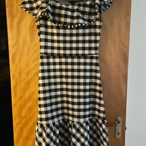 Off shoulder Svartvit rutig klänning med volang - Säljer en superfin svartvit rutig klänning med volangdetaljer. Den har en normal passform och är perfekt för både vår och sommar. Klänningen är ärmlös och har en söt volang upptill som ger en extra touch. Perfekt för en picknick eller en dag på stan!