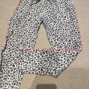 Leopardmönstrade byxor från Kiwi  - Säljer ett par leopardmönstrade byxor från Kiwi Saint-Tropez. De är grå med svarta och rosa detaljer och har en bekväm passform. 