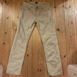 Lee byxor  - Säljer ett par snygga beige byxor från Lee i storlek herr M. De är i mycket bra skick och gjorda av 98% bomull och 2% elastan, vilket gör dem både bekväma och stretchiga. Perfekta för både vardag och lite finare tillfällen. (Ändå bra beskrivet av AI)
