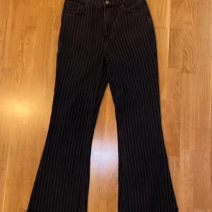 Svarta randiga byxor - Säljer ett par snygga svarta byxor med vita ränder. De är högmidjade och har en bootcut-stil som ger en retro vibe. Perfekta för både vardag och fest! 🖤Dem är i storleken w28, dem är långa i storleken då jag är 175 och dem går ner till hälarna på mig!