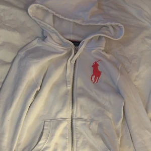 Vit hoodie från Ralph Lauren🪽🪽 - Säljer en snygg vit hoodie från Ralph Lauren med en stor röd logga på bröstet. Den har dragkedja och en skön huva. 