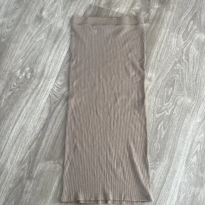 Beige ribbad långkjol - Säljer en superfin beige ribbad långkjol som är perfekt för både vardag och fest. Kjolen har en tight passform och är gjord i ett mjukt och stretchigt material som formar sig snyggt efter kroppen. Den neutrala färgen gör den lätt att matcha med olika toppar och accessoarer. Perfekt för höst och vår!