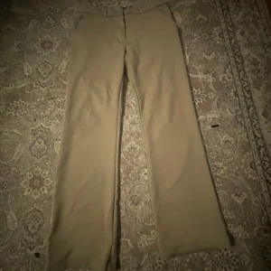 Beige kostymbyxor - Säljer ett par stilrena beige kostymbyxor i mycket bra skick. De har en klassisk design med knapp. Perfekta för både kontoret och mer formella tillfällen. Passformen är normal och materialet känns bekvämt och hållbart.