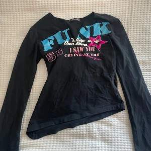 Svart långärmad tröja från Bershka - Säljer en cool svart långärmad tröja från Bershka med färgglada tryck och text på framsidan. Tröjan har en normal passform och är perfekt för en avslappnad stil. Den har detaljer i blått och rosa som verkligen poppar!