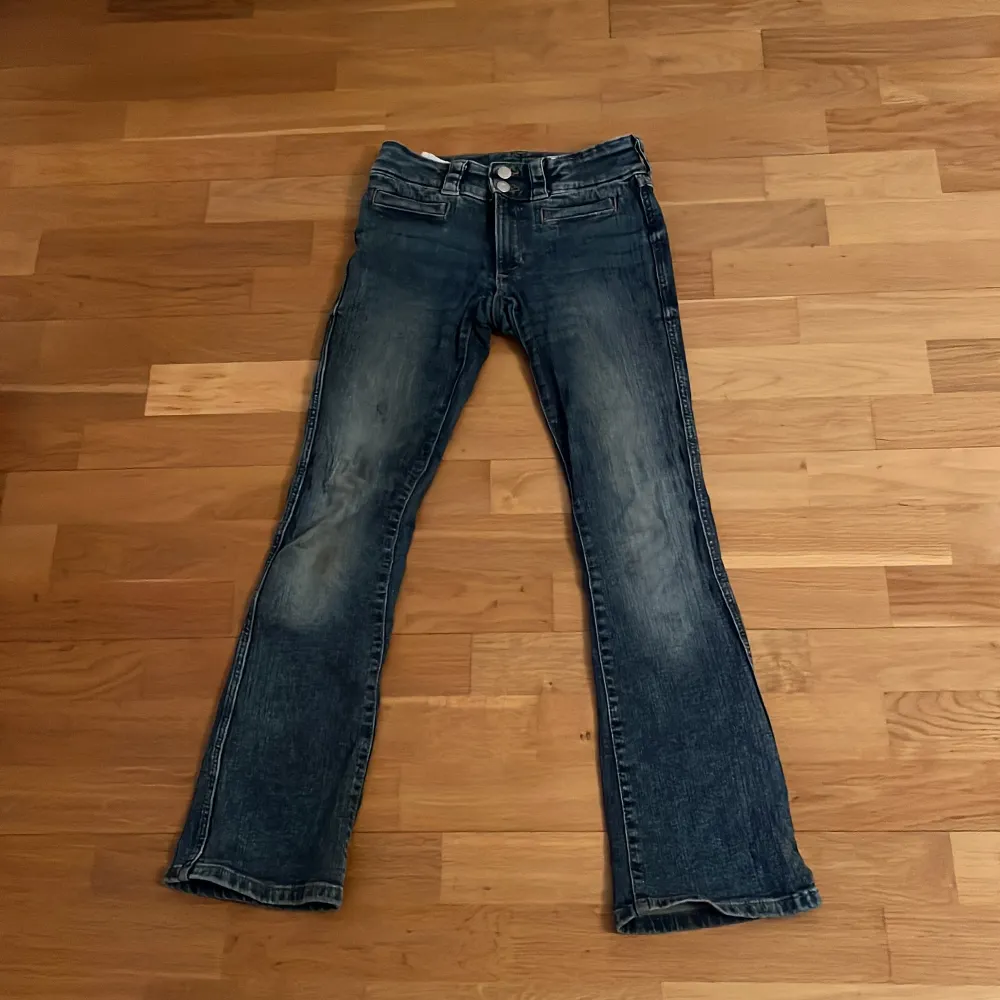 Säljer ett par snygga blå bootcut jeans. De har en klassisk femficksdesign med knappar och dragkedja fram. Är lite trasiga vid högra knät.. Jeans & Byxor.