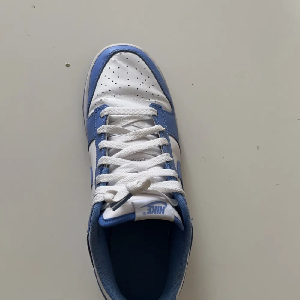 Säljer ett par snygga Nike Dunk sneakers i blått och vitt. De är helt nya och används bara 2 gånger. Skorna har en klassisk design med snörning och perforerad tå för extra ventilation. Perfekta för både vardag och träning!. Skor.