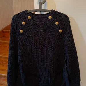 Poncho från Hunkydory - Stickad poncho i marinblå bomull med guldfärgade knappar. Mycket skön och snygg. Perfekt att dra på istället för en kofta. Mycket gott skick. Passar storlek S. 