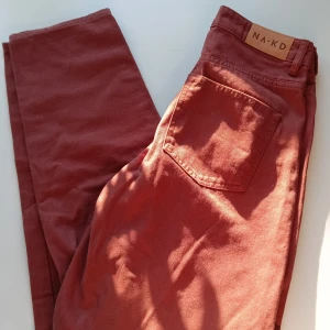 Bruna byxor från NA-KD - Säljer ett par snygga bruna byxor från NA-KD. De är högmidjade och har en klassisk femficksdesign med dragkedja och knapp framtill. Perfekta för både vardag och fest!