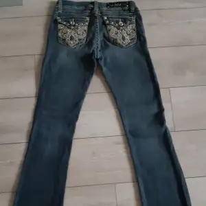 Säljer ett par snygga jeans med unika broderade detaljer på bakfickorna. De är mörkblå och har en tight passform med utsvängda ben. Lågmidjade.Perfekta för att ge din outfit lite extra bling! 💎