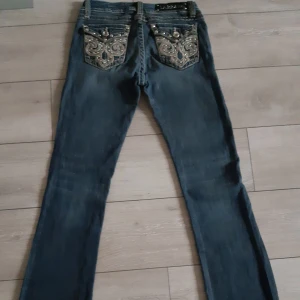 Jeans med broderade bakfickor - Säljer ett par snygga jeans med unika broderade detaljer på bakfickorna. De är mörkblå och har en tight passform med utsvängda ben. Lågmidjade.Perfekta för att ge din outfit lite extra bling! 💎