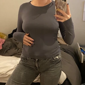 Mörkgrå långärmad tröja - Långarmad lite tajtare långärmad tröja jättelik den virala skimströjan. Perfekt till vardag. Tröjan har en tight passform som framhäver figuren och är gjord i ett mjukt och stretchigt material.