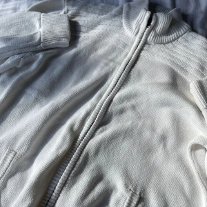 Vit stickad jacka med dragkedja - Säljer en superfin vit stickad kofta med dragkedja. Den har en ribbad krage och långa ärmar, perfekt för kyliga dagar. Jackan är i bra skick och passar både till vardags och lite finare tillfällen. Den är mjuk och bekväm, och ger en stilren look.