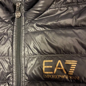 Svart quiltad jacka från Emporio Armani - Säljer en snygg lättviktsjacka från Emporio Armani EA7. Dragkedja framtill och är perfekt för höst och vår. Jackan är i fint skick och har en stilren design med EA7-loggan på bröstet. 