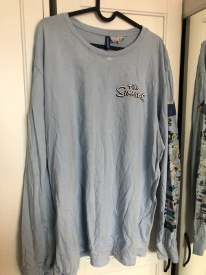 Simpsons tröja blå - Blå Simpsons långärmad tröja med motiv på armar och bröst. Väl använd men har inga defekter. Passar utmärkt till grunge inspirerande outfits  Kommer från rökfritt hem   Varan är tvättad 