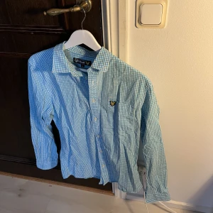 Lyle&Scott skjorta - Rutig ljusblå/vit skjorta från Lyle&Scott i väldigt bra skick endast använd någon gång, sedan legat i garderob därav lite skrynklig men en strykning och som ny.