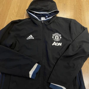 Manchester United Jacka - Manchester United vindjacka i storlek L. Helt oanvänd och är i bra skick.   Möts och fraktar, öppen för bud och hör av dig ifall du är intresserad!