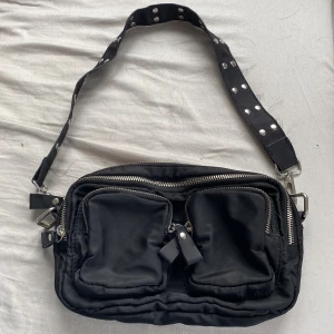 Gina tricot väska - Gina tricot väska som inte säljs längre, i svart tyg med ett axelband med nitar. Väskan har 5 fack.