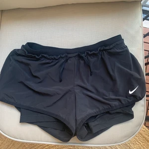 Nike träningsshorts strl S - Svarta shorts från Nike, strl S. Skulle säga de e normala i storleken. Low Rise på dessa. Sidorna på yttershortsen sitter inte ihop (se bild) så de är väldigt rörliga! Underbyxorna sitter fast i shortsen. Går att dra åt med snörena. De har även fickor.