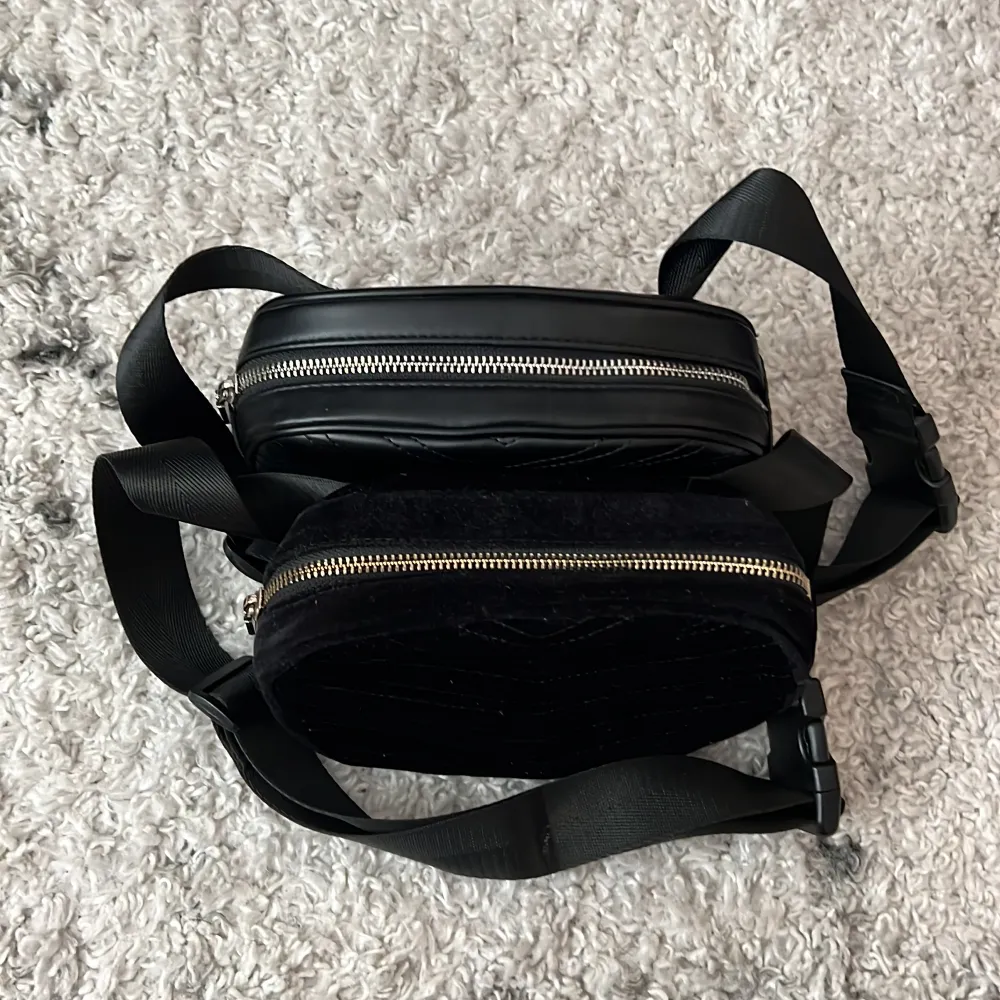 Svarta magväskor från H&M. Den ena är i imitations läder och den andra i sammet. Som nya.   19 cm breda och 12 cm höga.   Båda för 50 kr. Väskor.