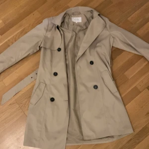 Beige trenchcoat, stilren  - Beige trenchcoat från vila, kommer över knäna. Lätt och elegant, stil ren. Använts en gång 