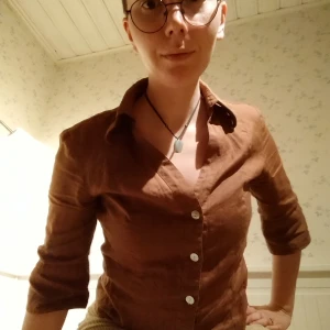 Brun figursydd skjorta - Brun skjorta i 55% linne (går inte att läsa resten men gissar på polyester). V-ringad med kvartsärmar. Figurnära och sitter fint. Vackra pärlemorfärgade knappar. Obs knapparna på vänster ärm sitter löst, se sista bilden.