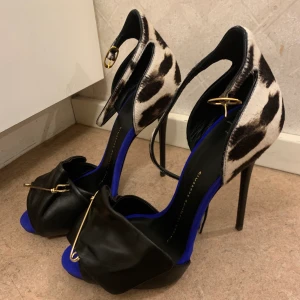 Giuseppe Zanotti klackskor med leopardtryck - Svarta klackar från Giuseppe Zanotti design. Detaljer i blått, guld & säkerhetsnål fram. Finns ett leopardtryck vid hälen & på bandet vid ankeln. Klackhöjd: 12cm. Använda en gång, i gott skick. Kan mötas upp i Stockholm eller skicka dem, du betalar frakt.