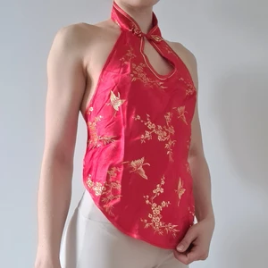 Kinesisk halterneck topp med öppen rygg - Unik, vacker, röd, kinesisk halterneck topp med öppen rygg. Knyts med ett tunt band i ryggen. Knäppning vid halsen. Säljer en likadan i mörkblå. Buren av en harpist vid Kungliga Hovkapellet.