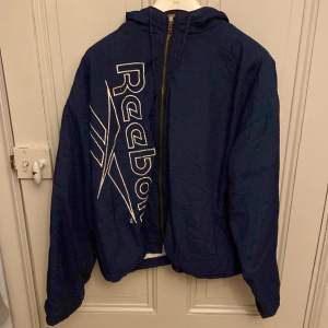 Blå vintage Reebok jacka, har ett litet färgfel på loggan (bild 3). Köpt på seamsvintage i Stockholm och har en skön cropped fit.