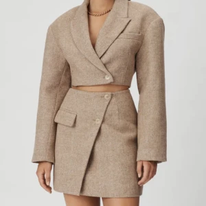 Adoore set - HELT NYTT!! Adoore set strl XS  Croppad kavaj i beigemelerad. Kavajen har boxig överdimensionerade axlar, en avskuren längd och knappar vid manschetten.   Kostym minikjol i beigemelerad. Den här kjolen har en stängning med två knappar vid manchetten. 