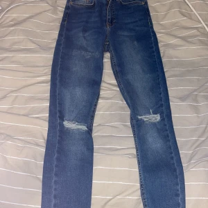 Jeans med slitningar  - Blåa jeans som är använda 1 gång. Slitningar vid knäna. Stretchiga så passar 32 och även 34